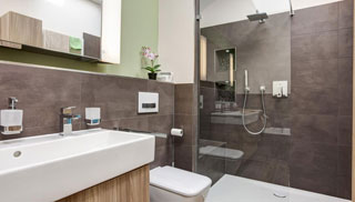 Zu sehen ist ein Modernes Bad mit langem Waschbecken, Toilette und Dusche.  Die Wände sind mit dunklen Fliesen gefliest.